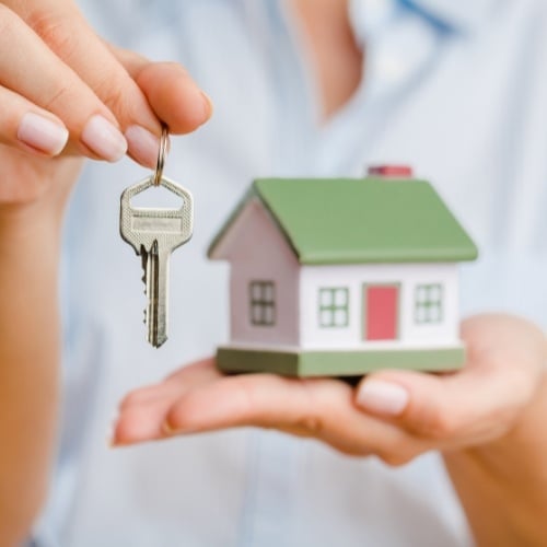 person holding a house figurine and a key