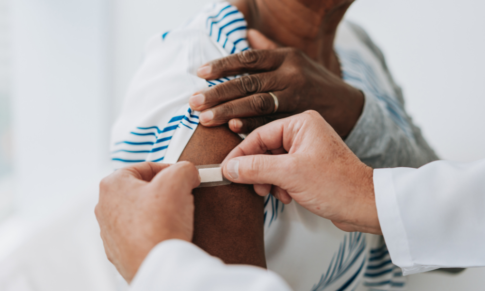 doctor placing a bandaid on a patient's shoulder after giving them a vaccine