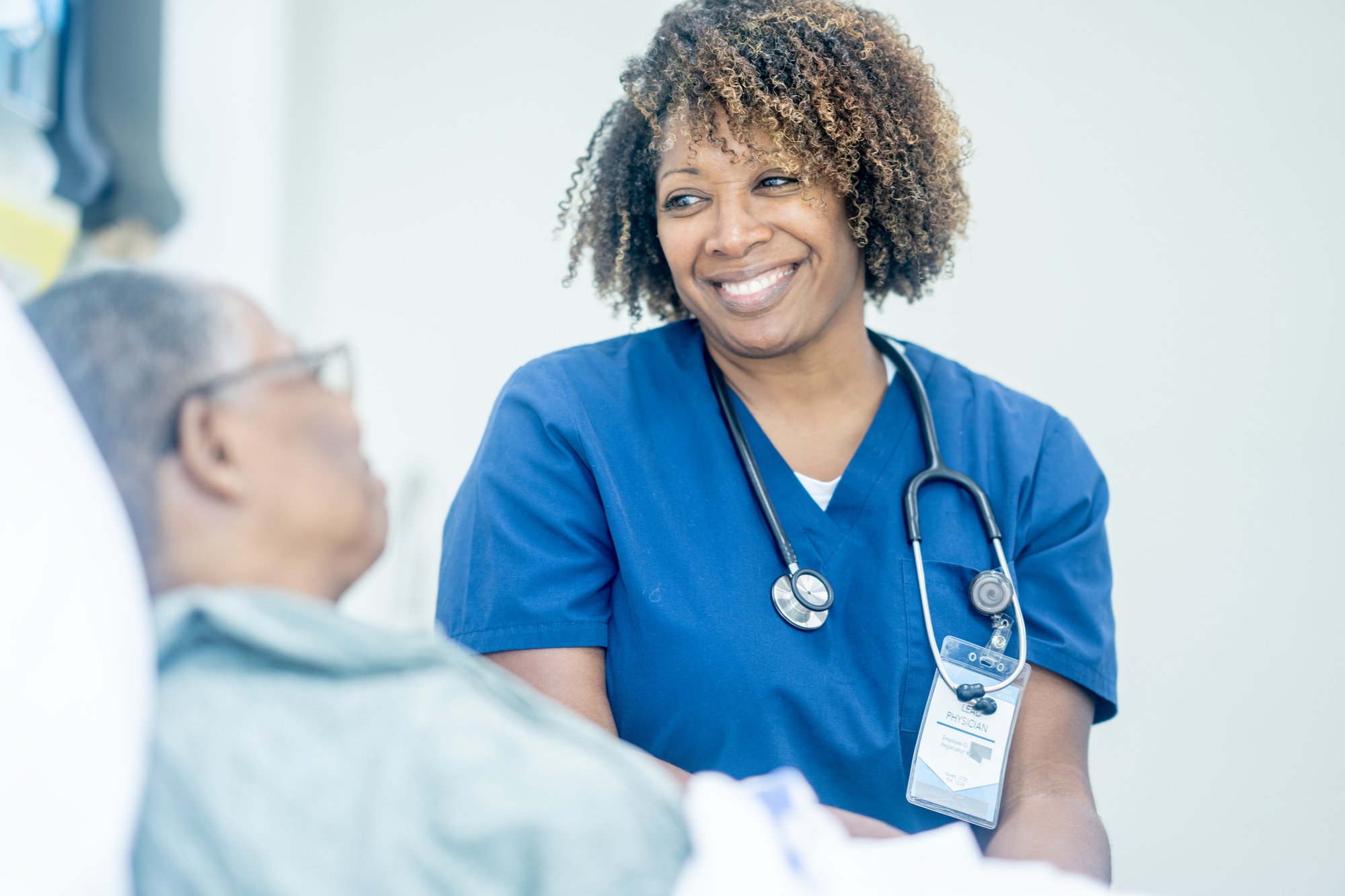 A healthcare provider sits at the bedside of an elderly person