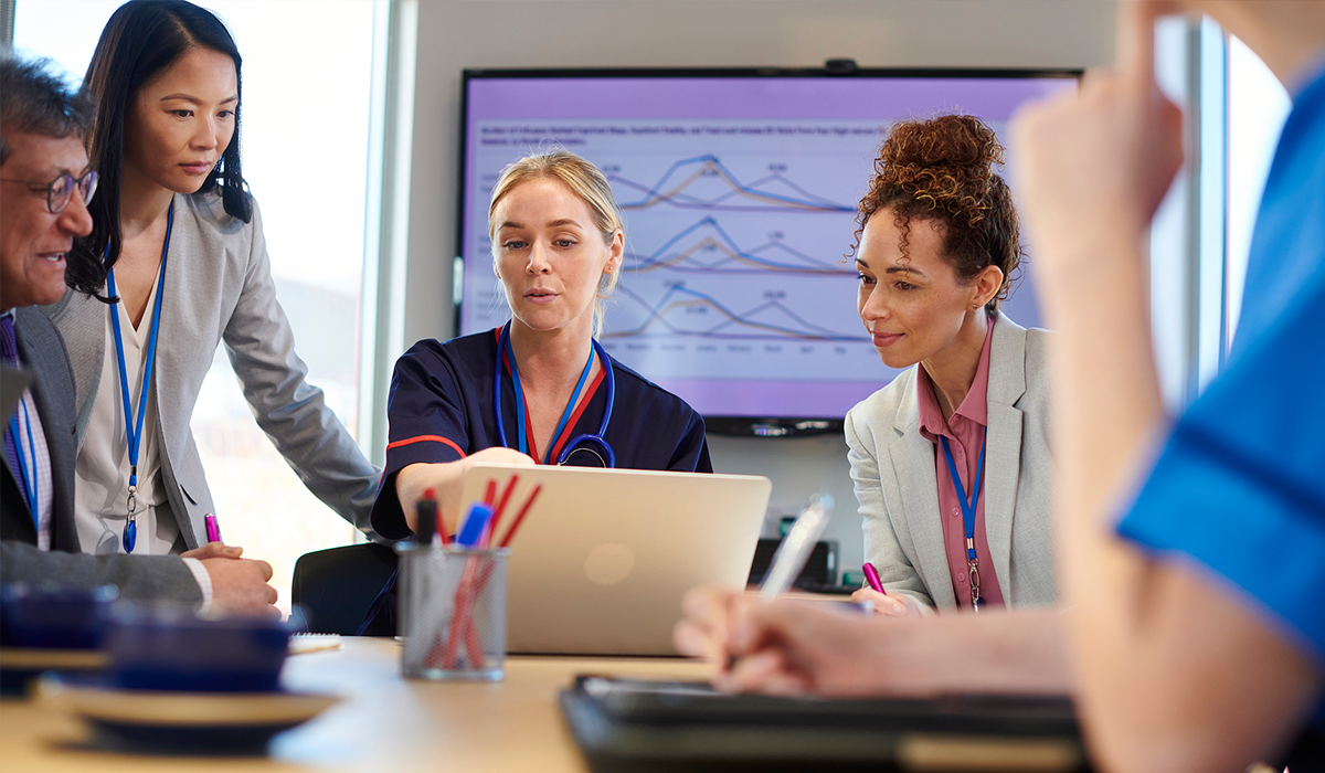 Healthcare workers gather around a computer and talk